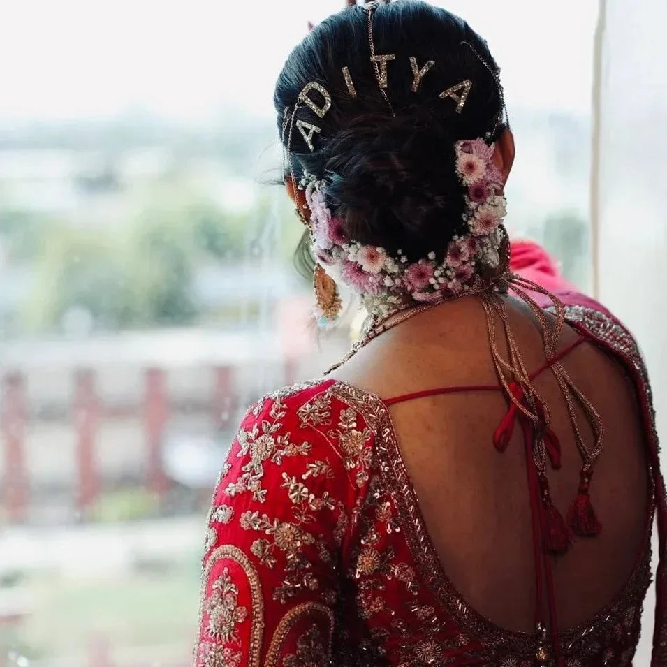 Bride wearing gold ADITYA letter pins above a floral bun with a red bridal outfit