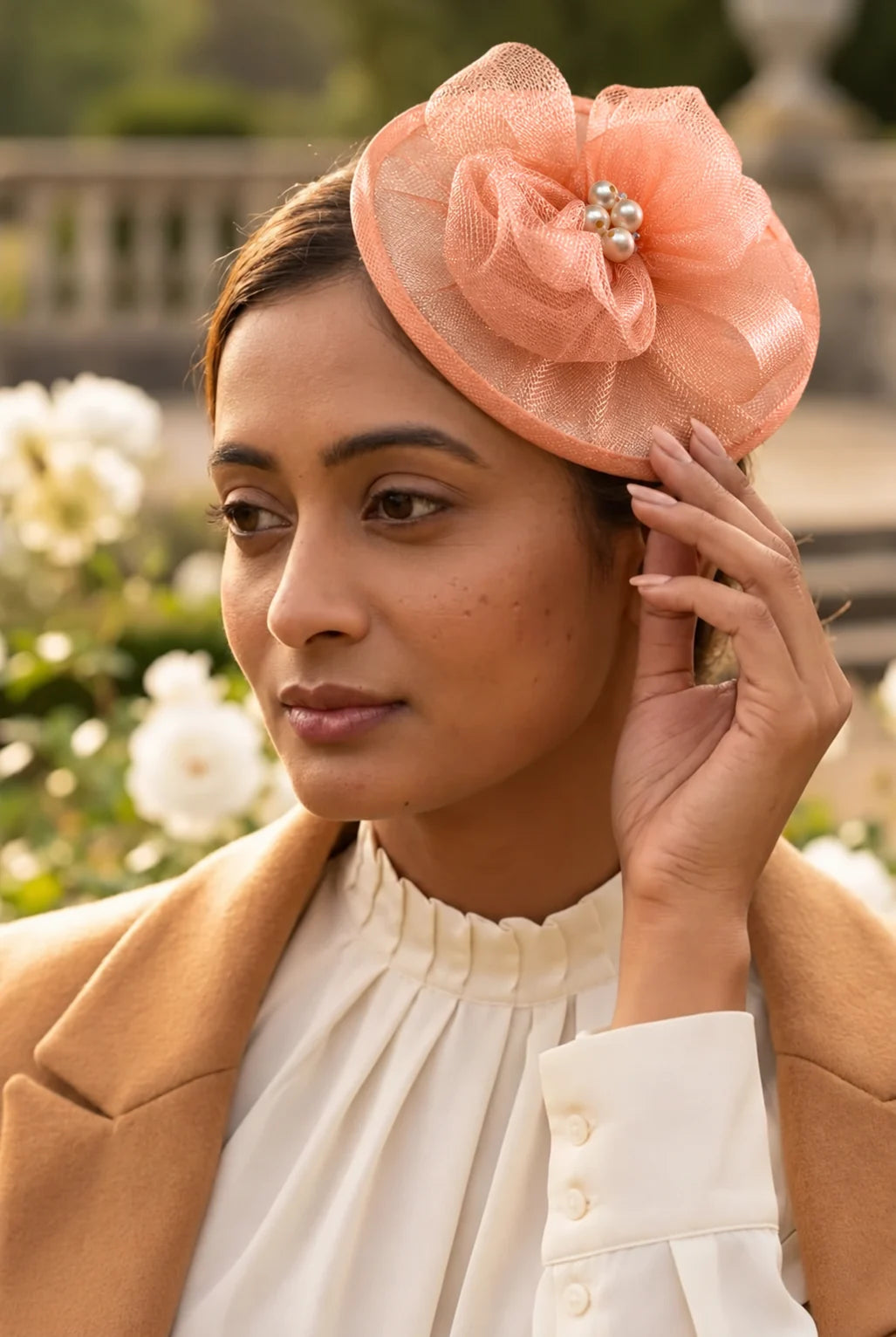 Close-up of a woman wearing the Elaria Vintage Peach Fascinator with peach mesh loops and pearl centre in a garden.